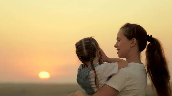 Mamá juega con su hija y le muestra al niño la puesta de sol. Familia feliz, mamá e hija en el campo miran al sol. El concepto de una familia feliz y niños sanos. bebé ama mami —  Fotos de Stock