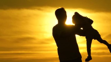 Baba, sevgili sağlıklı kızını kollarının arasına alıyor. Gün batımında baba ve çocuğun silueti. Mutlu baba ve küçük çocuk parkta gün ışığında oynuyorlar. Aile tatilde. çocukluk