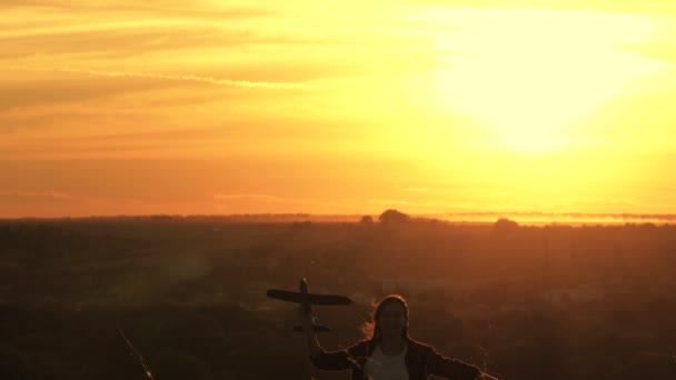 Fille heureuse court avec un avion jouet sur un terrain dans la lumière du coucher du soleil. La fille veut devenir pilote et astronaute. Au ralenti. Les enfants jouent au jouet avion. Adolescent rêve de voler et de devenir pilote. — Video