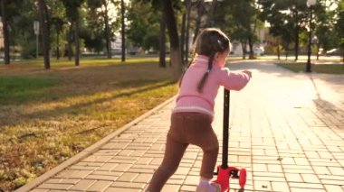 Küçük kız scooter sürmeyi öğreniyor. Parkta oynayan mutlu bir kız bebek. Sağlıklı bir çocuk sokakta scooter 'a biniyor. Mutlu çocukluk kavramı