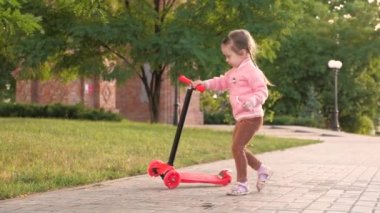 Küçük kız scooter sürmeyi öğreniyor. Parkta oynayan mutlu bir kız bebek. Sağlıklı bir çocuk sokakta scooter 'a biniyor. Mutlu çocukluk kavramı