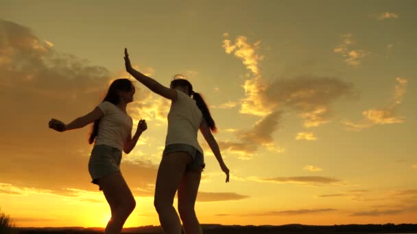 Chicas libres están bailando alegremente en una noche de verano al atardecer. celebración al aire libre. Celebra un día de verano con una fiesta en la playa. adolescentes sanos levantan alegremente las manos. vacaciones divertidas en la orilla — Vídeo de stock