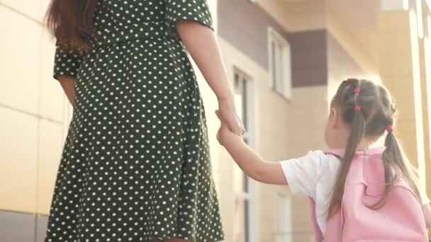 Kleine Tochter Schulmädchen geht mit einem Rucksack und hält ihre Mutter Hand. Vorschulpädagogisches Konzept. Glückliche Familienmutter und Kind gehen Händchen haltend zur Schule. — Stockvideo