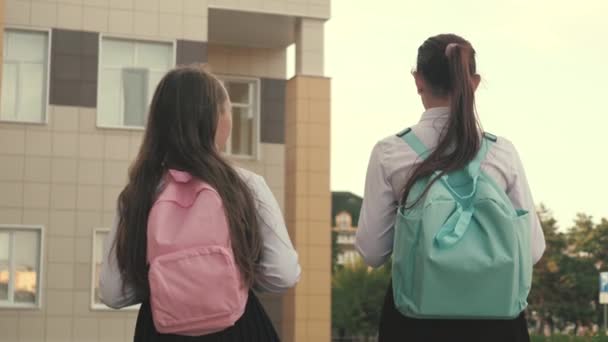 Schoolgirls with backpacks go to school on street. girlfriends go to school. They have a lot of fun. education concept. healthy teenagers go to class outdoors. girls chat and talk in the schoolyard — Stock Video