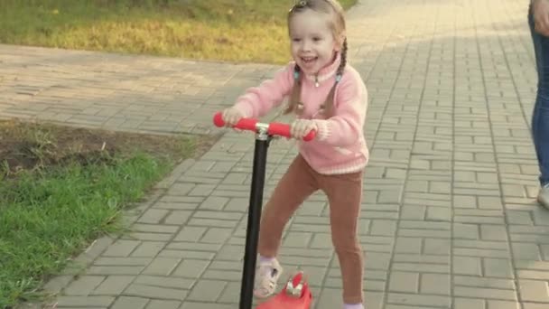 Küçük kız scooter sürmeyi öğreniyor. Parkta oynayan mutlu bir kız bebek. Sağlıklı bir çocuk sokakta scooter 'a biniyor. Mutlu çocukluk kavramı — Stok video