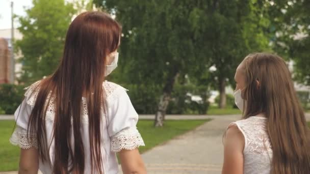 Två flickor i skyddsmasker går på sina ansikten utomhus i parken. skydda turister från virus. Tonåringar på gatan i staden reser i medicinsk mask. utomhus masker för att skydda mot infektion — Stockvideo