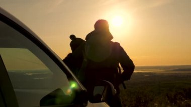 Mutlu gezginler arabanın yanında durur ve tepeden gün batımını seyrederler. Turistler gün doğumunu, ormanı ve nehri hayranlıkla seyrederek arabayla seyahat ederler. Özgür gezginler, turistler.