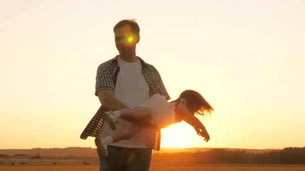 Papà sta circondando la sua amata figlia tra le sue braccia, un bambino sano sorride in volo. Bambino felice gioca con suo padre al tramonto sul campo. Papa 'e bambino nel parco estivo. famiglia sana e infanzia — Video Stock