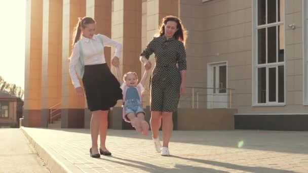 En frisk liten dotter leker med sin mor och syster, håller sina händer och hoppar. familje- och barndomskoncept. Glada barnhoppning. lycklig familj, mor och barn går till skolan innehav — Stockvideo