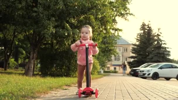 Dziewczynka uczy się jeździć na skuterze. szczęśliwa dziewczynka bawiąca się w parku. zdrowe dziecko jeździ skuterem po mieście na ulicy. szczęśliwy pomysł dzieciństwa — Wideo stockowe