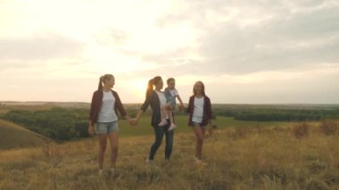 Mutlu çocuklar ve ebeveynler güzel güneş ışınlarında yürürler, tatile çıkarlar. Sağlıklı, gülümseyen bir aile gün batımında tarlada yürürken annelerinin kucağında küçük bir kız..