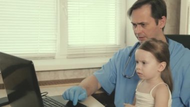 Profesyonel erkek doktor çocuk doktoru, tatlı anaokulu çocuğuyla oynayan ve dizüstü bilgisayarda çalışan. Hasta kız çocuk doktorunun kucağına oturuyor. Çocukların tedavisi için pediatrik muayene kavramı