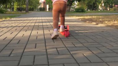 Küçük kız scooter sürmeyi öğreniyor. Parkta oynayan mutlu bir kız bebek. Sağlıklı bir çocuk sokakta scooter 'a biniyor. Mutlu çocukluk kavramı