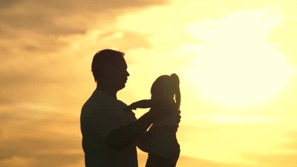 Papa umkreist seine geliebte gesunde Tochter auf dem Arm. Silhouette von Vater und Kind bei Sonnenuntergang. glücklicher Vater und kleines Kind, die sich im Park auf die Natur in den Strahlen der Sonne umarmen. Familie im Urlaub. — Stockvideo