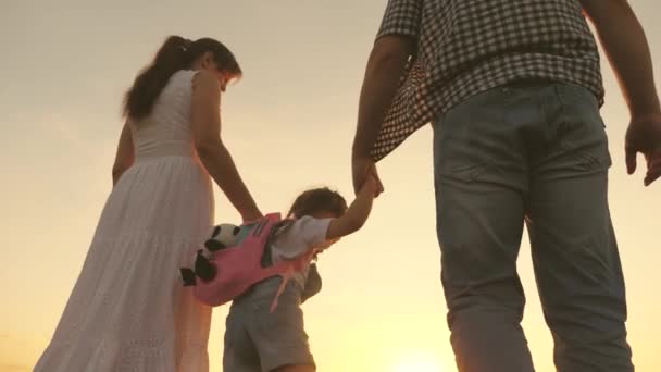 Gelukkige familie en kind loopt in het park bij zonsondergang. een vrolijk kind houdt zijn ouders handen vast en springt in zonnestralen. Mam, pap en dochter zijn blij om in het veld te lopen. Gelukkig en gezond familieconcept — Stockvideo