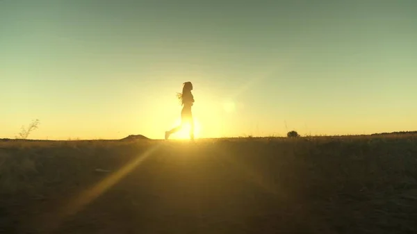 Correr tras el sol. Entrenamiento de trotar. Una hermosa chica sana se dedica a la aptitud física, trotar en el país en el sol. Chica corredora respira aire fresco en el campo. Mujer joven libre corre en el parque de verano al atardecer. — Foto de Stock