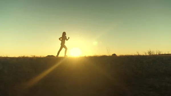 Güneşin peşinden koşmak. Antrenman koşusu. Sağlıklı, güzel bir kız spor yapıyor, kırsalda güneş altında koşuyor. Koşucu kız sahada temiz hava soluyor. Özgür genç kadın gün batımında yaz parkında koşuyor.. — Stok fotoğraf