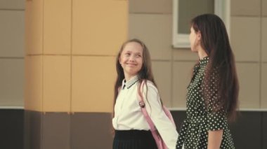 Anne ve kız öğrenci bir sırt çantasıyla gidip annelerinin elini tutuyor. Okul eğitimi konsepti. Mutlu aile annesi ve çocuğu el ele tutuşarak okula gider..