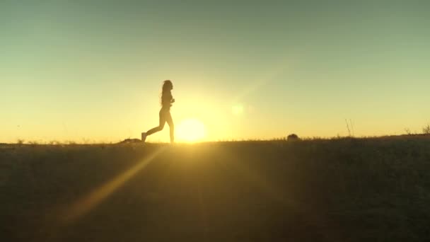 Güneşin peşinden koşmak. Antrenman koşusu. Sağlıklı, güzel bir kız spor yapıyor, kırsalda güneş altında koşuyor. Koşucu kız sahada temiz hava soluyor. Özgür genç kadın gün batımında yaz parkında koşuyor.. — Stok video
