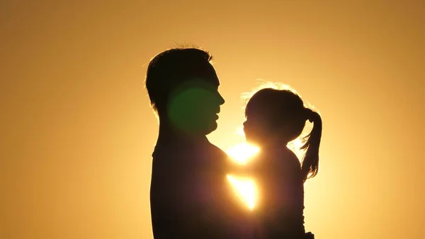 Papa encercle sa fille bien-aimée dans ses bras. silhouette de père et d'enfant au coucher du soleil. heureux père et petit enfant étreignant dans le parc sur la nature dans les rayons du soleil. famille en vacances. — Photo