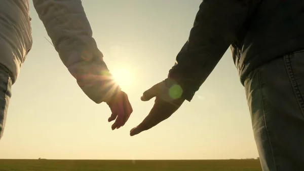 日没時に男と女の手。ヤシの木漏れ日。日没時に手をつなぐカップルを愛して。手を友人に伸ばせ。太陽光線が指を通して輝きます。愛、幸福と友情. — ストック写真