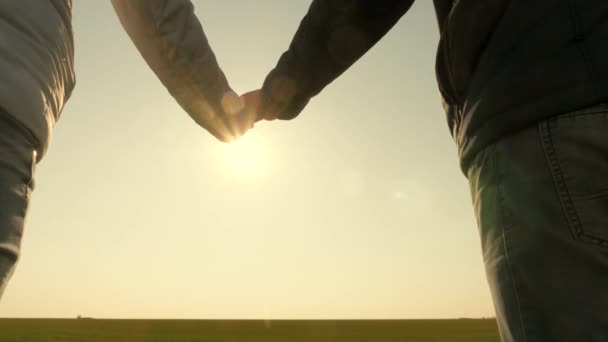 Τα χέρια του άντρα και της γυναίκας στο ηλιοβασίλεμα. ηλιόλουστη λάμψη στις παλάμες. Αγαπημένο ζευγάρι που κρατιέται χέρι-χέρι το ηλιοβασίλεμα. Απλώστε το χέρι σας σε ένα φίλο. Οι ακτίνες του ήλιου λάμπουν μέσα από τα δάχτυλά σου. Αγάπη, ευτυχία και φιλία. — Αρχείο Βίντεο
