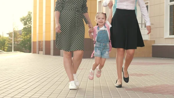 Familia feliz madre e hijos van a la escuela tomados de la mano. niña colegiala va con una mochila y toma de la mano de la madre y la hermana. concepto de educación escolar. niño alegre saltando —  Fotos de Stock