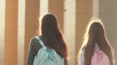 Anne ve kız öğrenci bir sırt çantasıyla gidip annelerinin elini tutuyor. Okul eğitimi konsepti. Mutlu aile annesi ve çocuğu el ele tutuşarak okula gider..