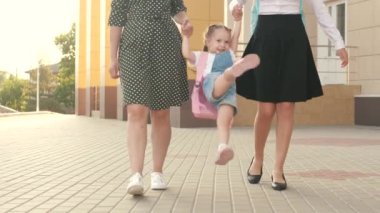 Mutlu aile anne ve çocukları el ele tutuşarak okula giderler. Küçük kız öğrenci bir sırt çantasıyla gider ve anne ve kız kardeşinin elini tutar. Okul eğitimi konsepti. Neşeli çocuk atlaması