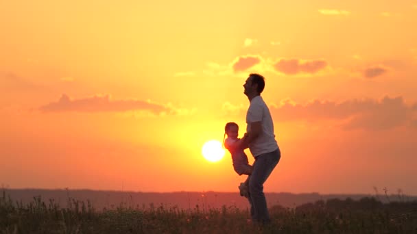 Papa joue avec sa petite fille, jette joyeusement l'enfant dans le ciel. famille heureuse dans la nature. Papa et enfant. famille se reposant au coucher du soleil dans le champ. famille heureuse et en bonne santé marchant dans l'air frais. — Video