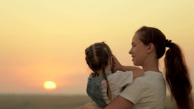 Anne kızıyla oynar ve çocuğa günbatımını gösterir. Mutlu aile, tarladaki anne ve kız güneşe bakıyor. Mutlu bir aile ve sağlıklı çocuklar kavramı. Bebek annesini seviyor.