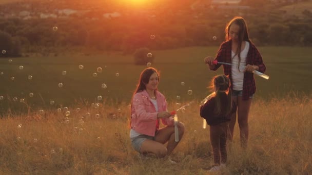 Blaas bubbels in de zon, kinderen verjaardagsfeestje. Gelukkige kinderen spelen samen, blazen en vangen zeepbellen. Zusters spelen samen in het park bij zonsondergang. Gelukkige familie en kind concept. — Stockvideo