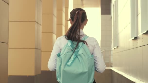 En skolflicka med ryggsäck går ner för gatan till skolan en vacker ung elev går till klassen. Begreppet utbildning. en tonårstjej skyndar till klassen. — Stockvideo