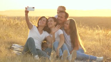 Mutlu aile yolculukları. Parktaki akıllı telefondan selfie. Anne, baba ve çocuklar battaniyenin üzerinde oturmuş video çekiyorlar. Anne ve baba kızlarıyla tarlada fotoğraf çekiliyor. blog yazarları ailesi