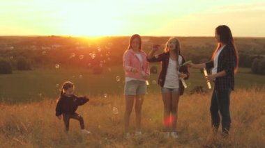 Güneşli hava kabarcıkları, çocukların doğum günleri. Sağlıklı çocuklar ve anne oynar, saksocu çocuk sabun köpüğü yakalar. Anne ve kız kardeşler gün batımında parkta birlikte oynuyorlar. Mutlu aile ve çocukluk kavramı