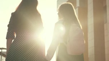 Mutlu aile anne ve çocuğu, güneş ışığında el ele tutuşarak okula giderler. Anne ve kız öğrenci bir sırt çantasıyla gidip annelerinin elini tutuyor. okul eğitimi kavramı.