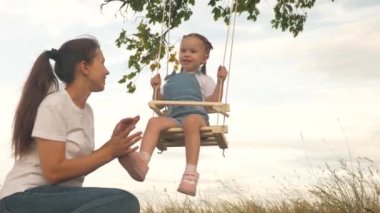Mutlu özgür aile parkta eğleniyor. Anne çocuğuyla oynuyor, parktaki bir ağaç dalında ipte sallanıyorlar. Anne, sağlıklı küçük kızını güneşin altında bir salıncakta sallıyor..