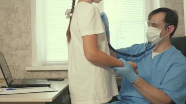 Erkek bir çocuk doktoru, çocuğun göğsüne steteskop uygular, genç bir kızın kalbini ve ciğerlerini dinler. Doktor çocuk doktoru çocuğu muayene ediyor. Doktor bebeğin kalp atışlarını dinler. Çocuk hastane odasında..