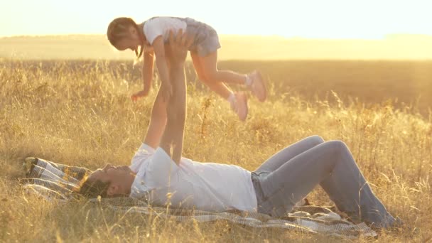 Papa 'gioca con la sua figlioletta nel parco su una coperta. papà vomita il bambino con le mani, il bambino è felice e ride. felice padre e bambino abbraccio nella natura al sole. famiglia in vacanza. — Video Stock
