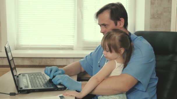 Barnundersökningskoncept för behandling av barn. Vårda professionell manlig läkare barnläkare, leka med söta förskola barn och arbetar på bärbar dator. flicka patient sitter i knät på barnläkare — Stockvideo