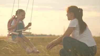 Özgür aile, parkta eğleniyor. Anne, sağlıklı küçük kızını güneşin altında bir ağacın altında sallıyor. Anne çocuğuyla oynuyor, ormanda meşe dalında sallanıyorlar..