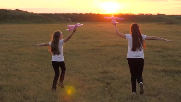 Sny o létání. Šťastné dětství. Dvě holky si při západu slunce hrají s letadýlkem. Děti na pozadí slunce s letadlem v ruce. Silueta dětí hrajících si v letadle — Stock video