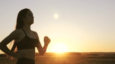 Antrenman koşusu. Sağlıklı, güzel bir kız spor yapıyor, kırsalda güneş altında koşuyor. Koşucu kız sahada temiz hava soluyor. Özgür genç kadın gün batımında yaz parkında koşuyor..