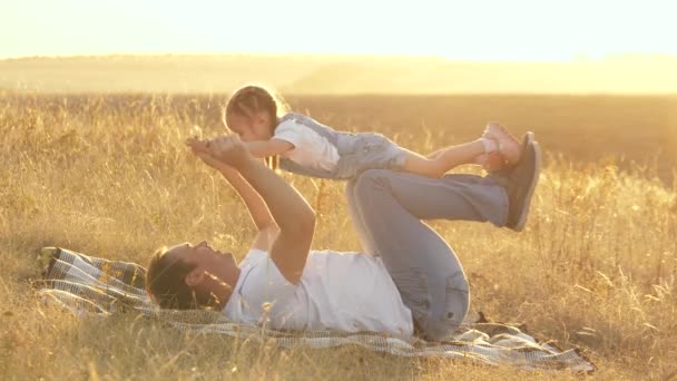Táta drží dítě v rukou, dítě lítá jako letadlo, raduje se a směje se. Táta si hraje se svou dcerou v parku na dece. šťastný otec a malé dítě objímající se v přírodě. rodina na dovolené. — Stock video
