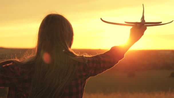 Chica quiere convertirse en piloto y astronauta. En cámara lenta. Chica feliz corre con un avión de juguete en un campo en la luz del atardecer. niños juegan juguete avión. adolescentes sueña con volar y convertirse en piloto. — Vídeos de Stock