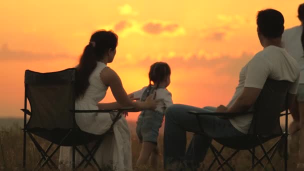 Silueta šťastné rodiny, matky, otce sedícího v turistických křeslech, tři děti si při západu slunce rády hrají. Máma a táta s dcerami, dovolená, kempování. rodinná letní dovolená — Stock video