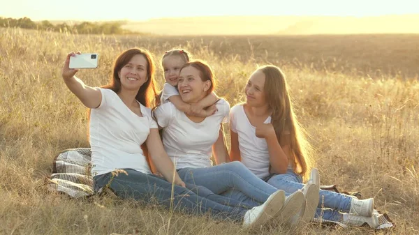 Šťastná rodina cestuje, selfie na smartphonu v parku. Máma a zdravé děti sedí na dece. matka se svými dcerami je fotografována na poli na přikrývce. rodinné cestování a dobrodružství — Stock fotografie