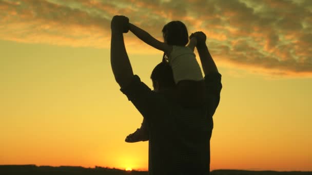 Papa loopt met zijn dochter op zijn schouders bij zonsondergang. Vader draagt schouders van zijn geliefde kind, in zonnestralen. kind met ouders loopt bij zonsondergang. gelukkige familie rust uit in het park. Papa. — Stockvideo