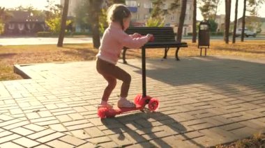 Küçük kız scooter sürmeyi öğreniyor. Parkta oynayan mutlu bir kız bebek. Sağlıklı bir çocuk sokakta scooter 'a biniyor. Mutlu çocukluk kavramı