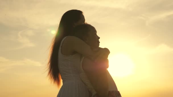 Família feliz mãe e filha em um campo ao pôr do sol. Mamãe abraços filha, eles admiram belo pôr do sol. conceito de família feliz de crianças e crianças. mãe e bebê caminham no parque, campo, ao sol — Vídeo de Stock